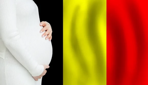Pregnant woman in a white knit sweater cradling her belly, with the Belgian flag's black, yellow, and red vertical stripes in the background.