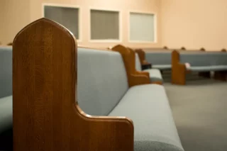 Empty church pews with wooden armrests and light blue upholstery in a quiet sanctuary